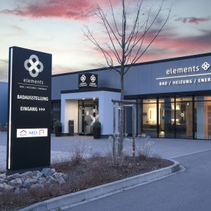 Die moderne Lichttechnik an der Firmenfassade in Siegen besteht aus einem beleuchteten 3D-Logo sowie einem dazu passenden Werbewürfel, der sich direkt über dem Eingangsbereich befindet.